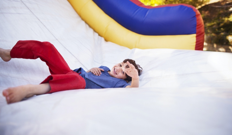 Happy Boy Playing On Bouncy Castle At Amusement Park